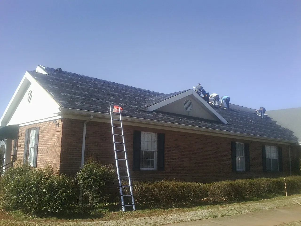Crew tearing shingles off a brick ranch roof with a ladder set — Emergency Roof Repair work by our crew in Norwalk